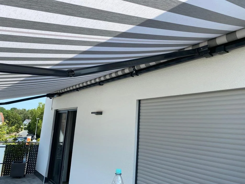 Balkon mit einem rollbaren Sonnenschutz mit grauen Streifen, über einem modernen weißen Gebäude mit Rollladen.