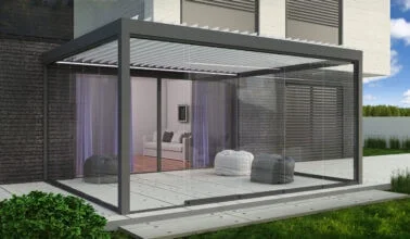 Moderne gläserne Veranda vor einem Haus, mit Sitzgelegenheiten und Vorhängen im Inneren.