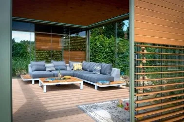 Moderner, offener Wohnzimmerbereich mit großen Fenstern, einem bequemen grauen Sofas, einem weißen Couchtisch und Blick ins Grüne im Hintergrund.