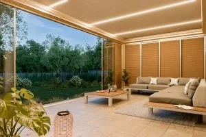 Moderne Wohnzimmer mit großen Glasfenstern, Sofa, Couchtisch und Blick auf einen Garten mit Bäumen bei Sonnenuntergang.