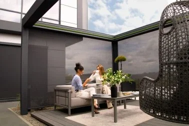 Drei Frauen sitzen auf einer Terrasse mit modernen Möbeln und grünem Blick nach draußen, neben einer Korbwinde.