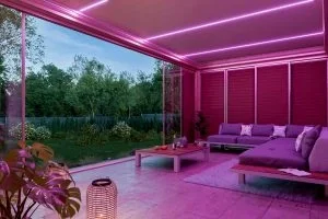 Innenraum eines modernen Wohnzimmers mit pinker Beleuchtung, großen Fenstern, Sofa und Couchtisch.