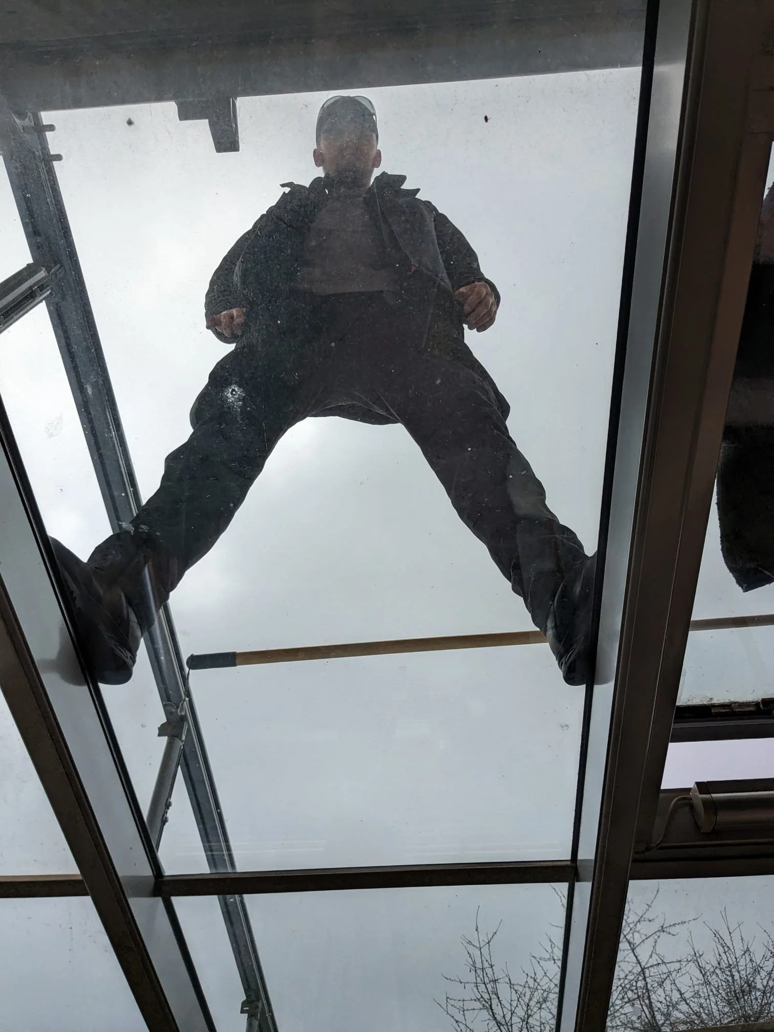 Blick nach unten auf eine Person, die auf dem Dach eines Gebäudes steht, mit Blick nach oben. Die Person trägt dunkle Kleidung und hat eine Tasche auf dem Rücken.