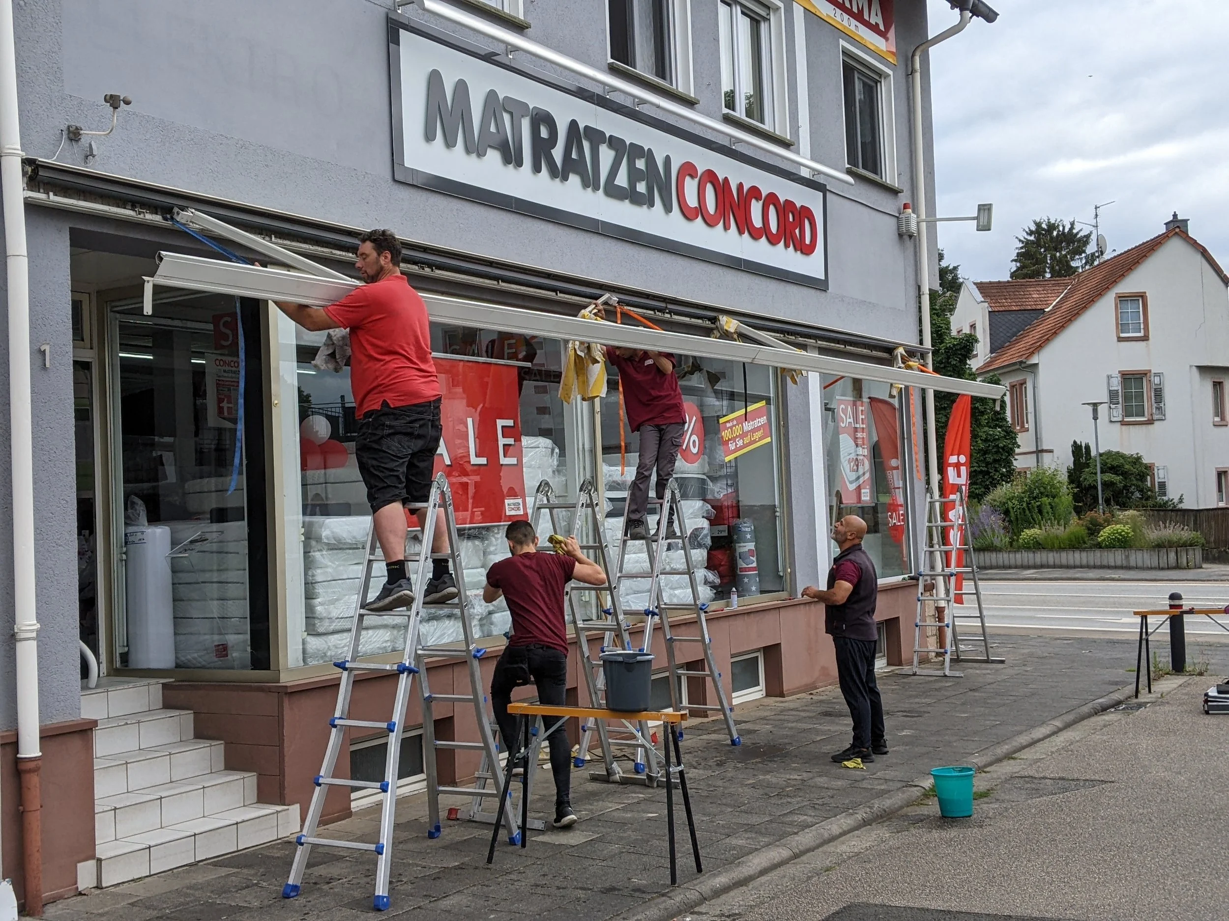 Vier Männer reinigen die Schaufenster eines Ladens namens 'MATRATZEN CONCORD'.