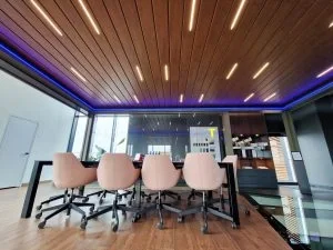 Ein moderner Konferenzraum mit einem langen Tisch und acht bequemen Stühlen, große Fenster mit Stadtblick, Holzdecke und LED-Beleuchtung.