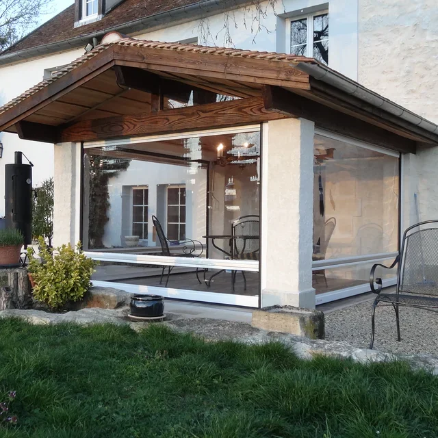 Ein gläserner Wintergarten an einem Haus mit Garten, inklusive Gartenmöbel und einer Pflanze im Topf.