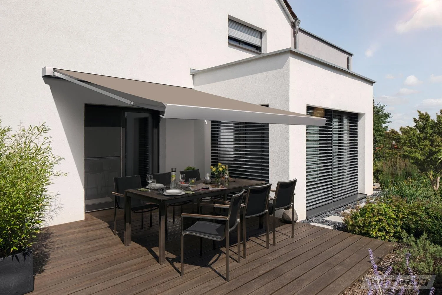 Moderner Balkon mit Esstisch und Stühlen vor weißem Haus mit Rollläden, umgeben von Garten mit Pflanzen und Bäumen bei sonnigem Himmel.