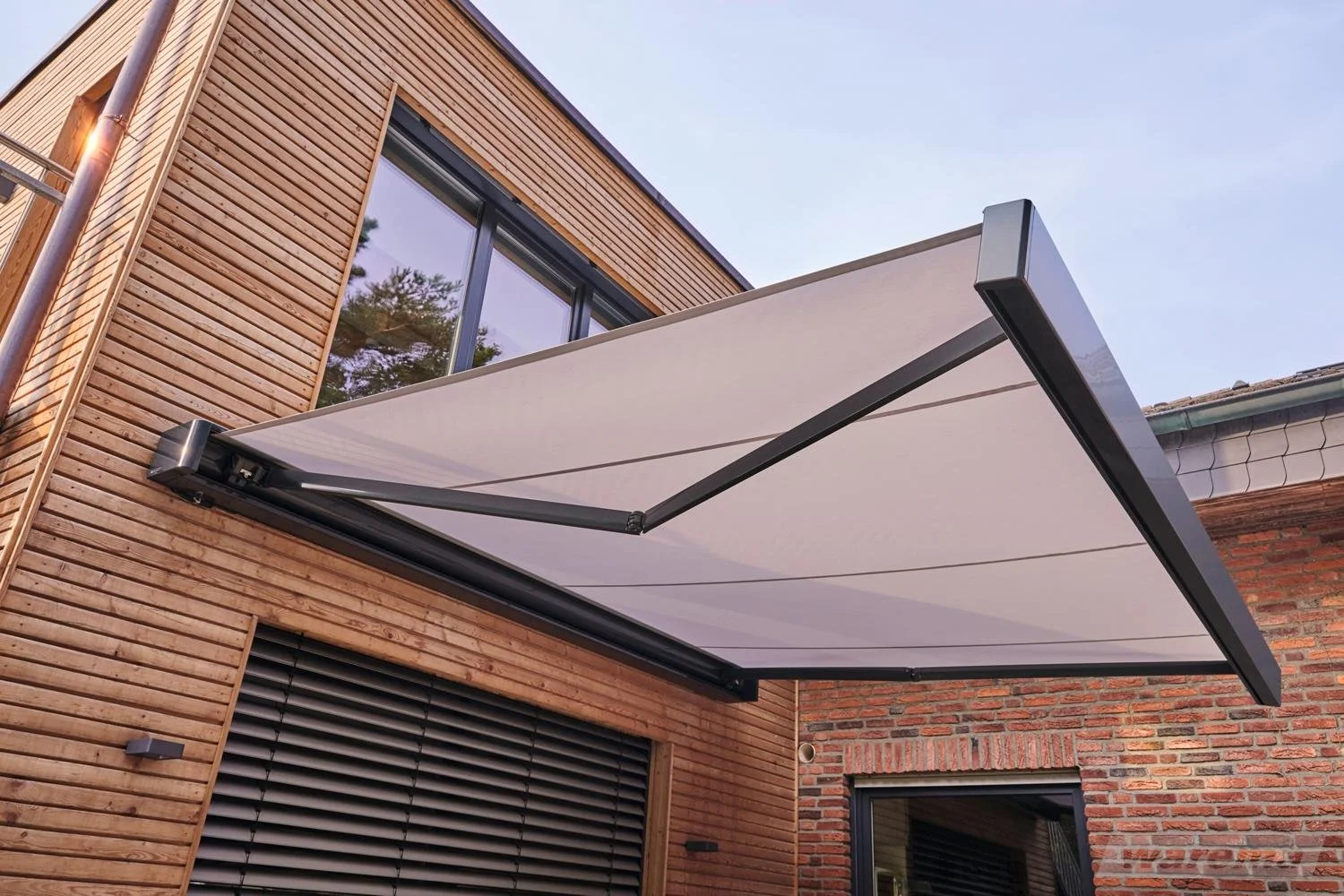 Ein moderner Hausvordach mit Sonnenschutz, aus Stoff mit schwarzem Rahmen, vor einem Haus mit Holz- und Ziegelsteinfassade.