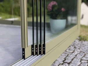 Nahaufnahme eines Fensterrahmens mit schwarzem Schiebermechanismus, im Hintergrund eine Pflanze in einem blauen Topf