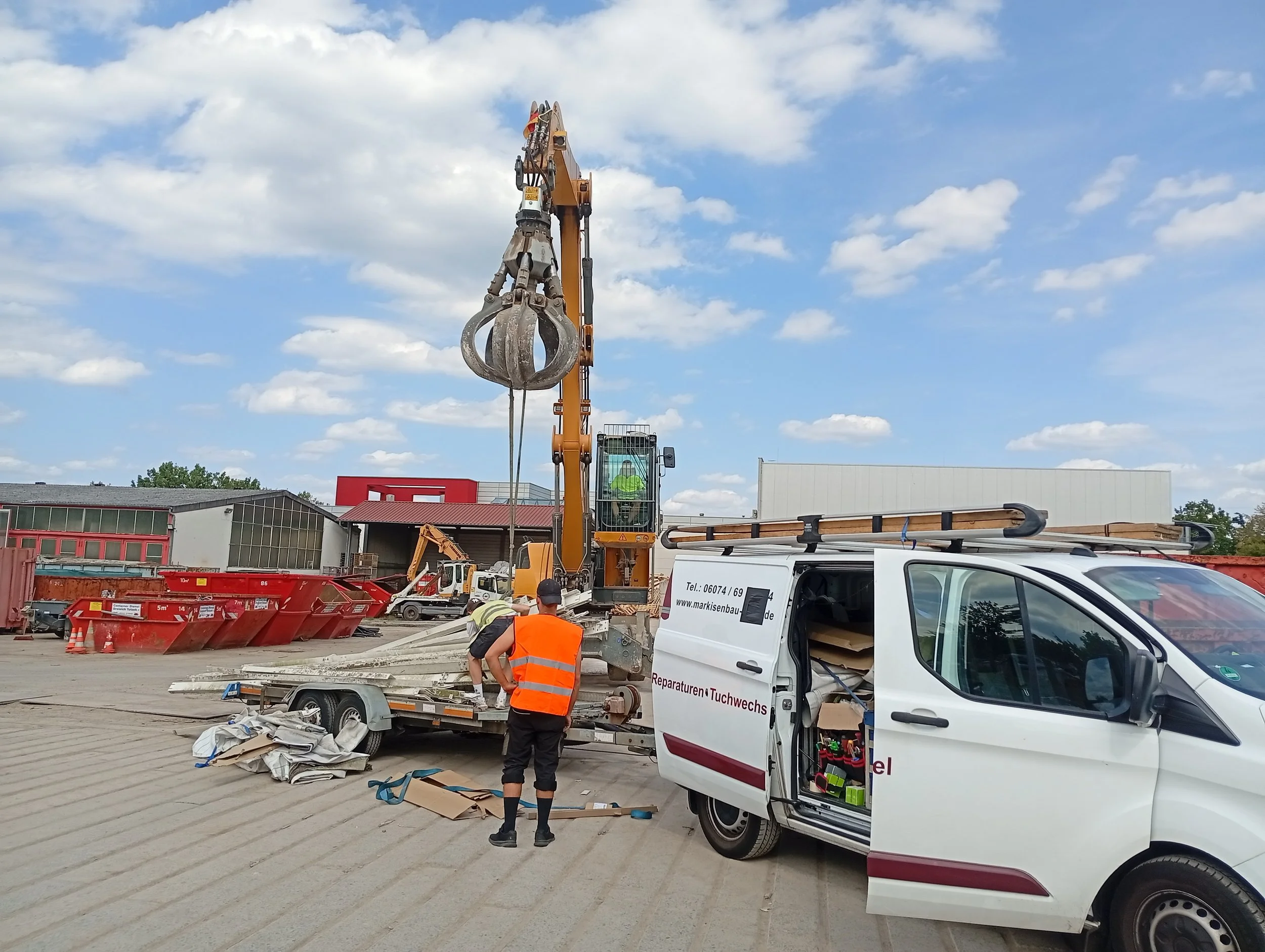 Bauarbeiter bei der Arbeit auf einer Baustelle mit Baustellenfahrzeugen, einem Kran, einem weißen Servicefahrzeug mit Werkzeugen, und einem roten Container im Hintergrund, bei sonnigem Himmel.
