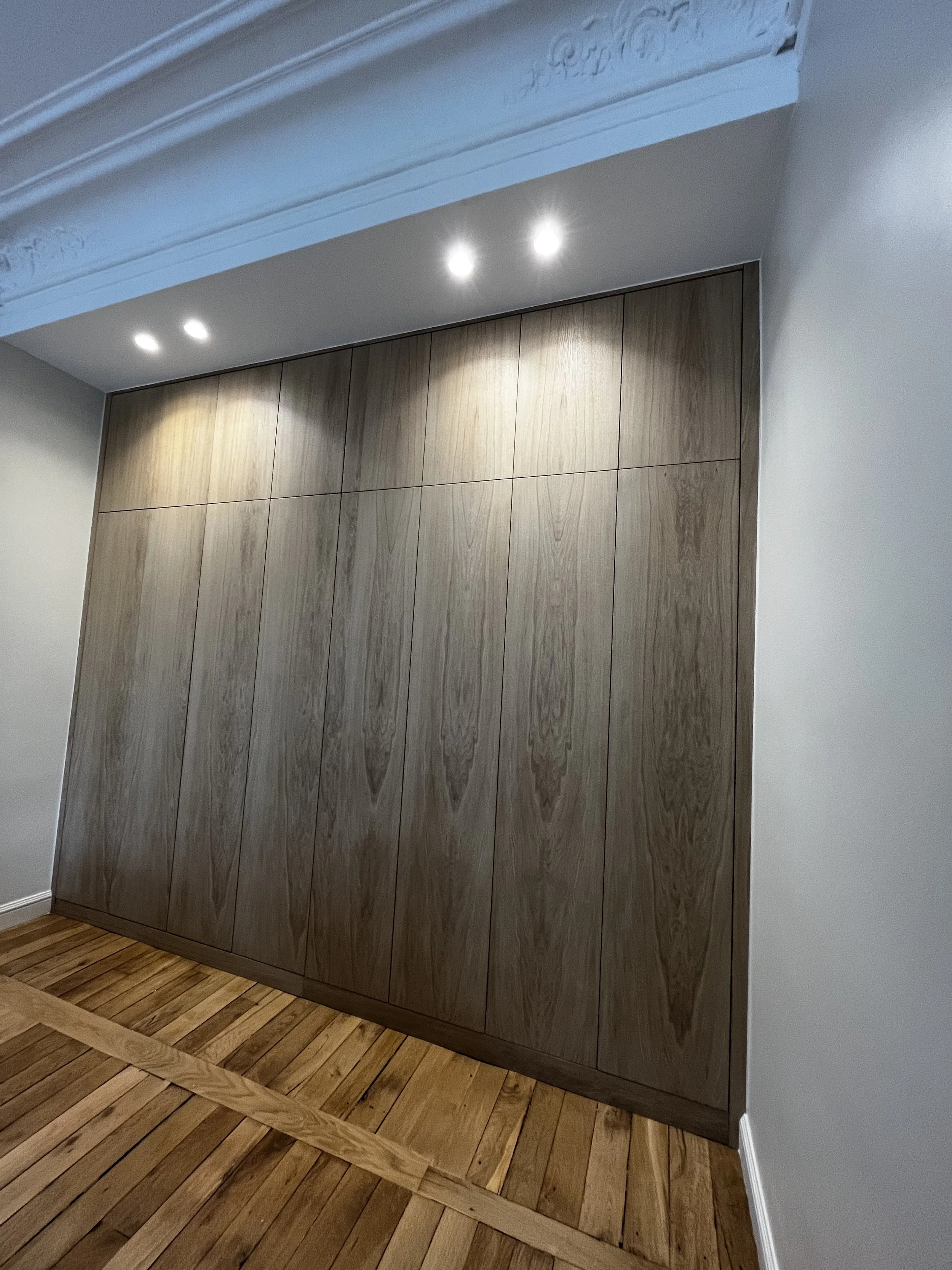 Un grand meuble de rangement en bois foncé avec plusieurs portes, installé dans un intérieur moderne. Le sol est en bois clair.