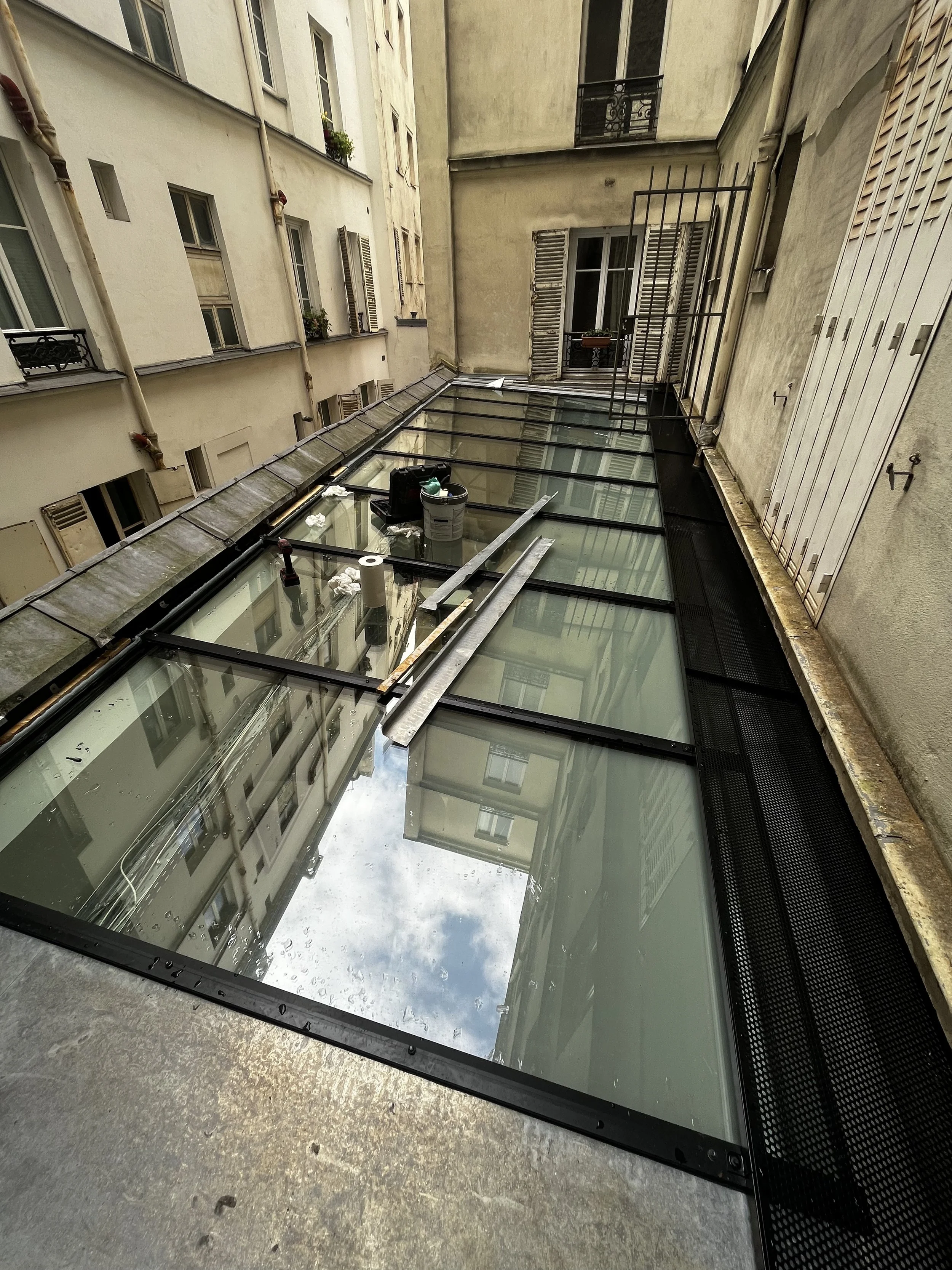 Rénovation d'une toiture en verre sur un bâtiment parisien, avec outils et matériel de construction sur place.
