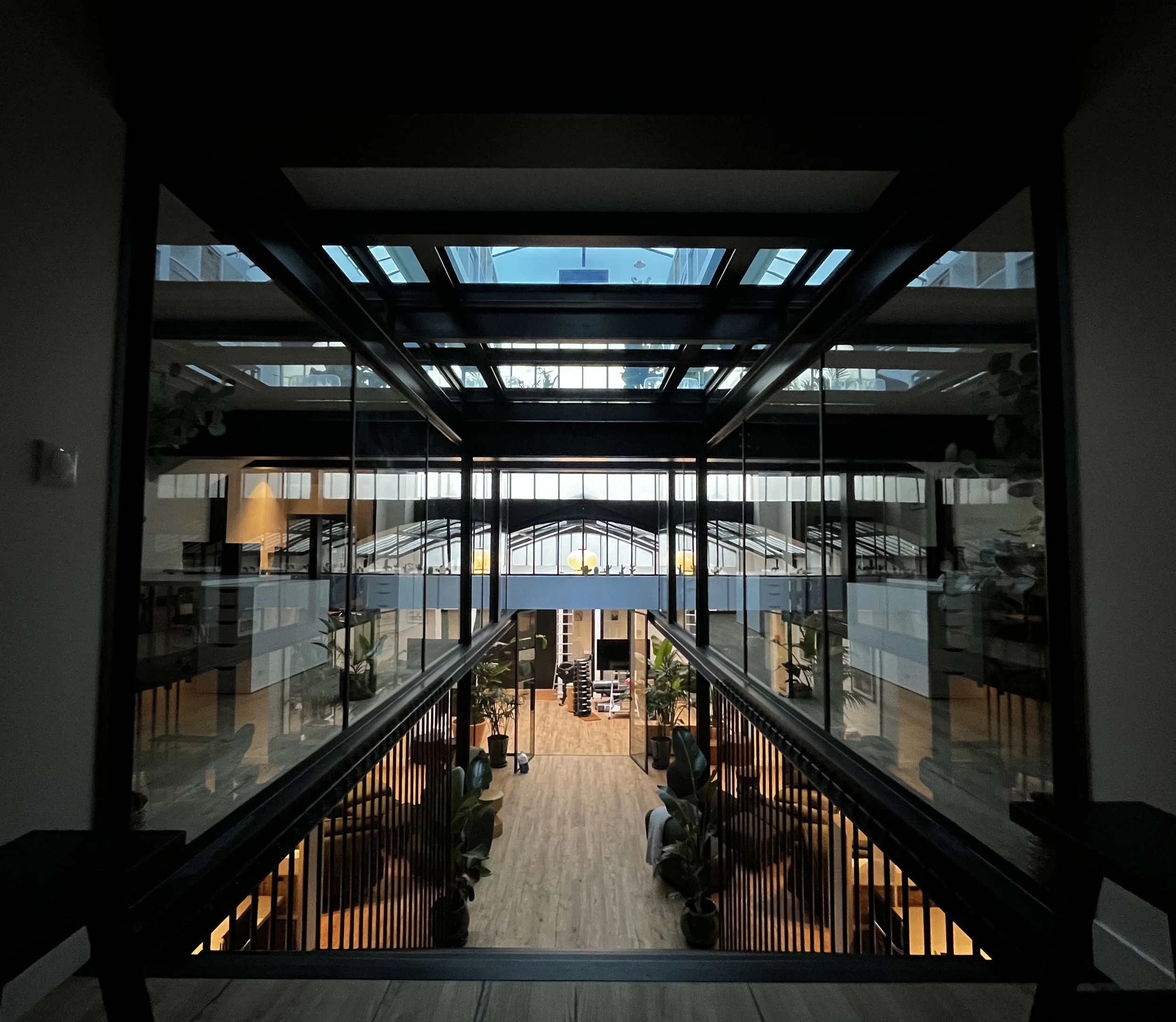 Vue intérieure d'une maison ou d'un bâtiment, vue à travers une grande baie vitrée ou un puits de lumière, avec des plantes et des meubles visibles à l'intérieur, ambiance moderne et lumineuse.