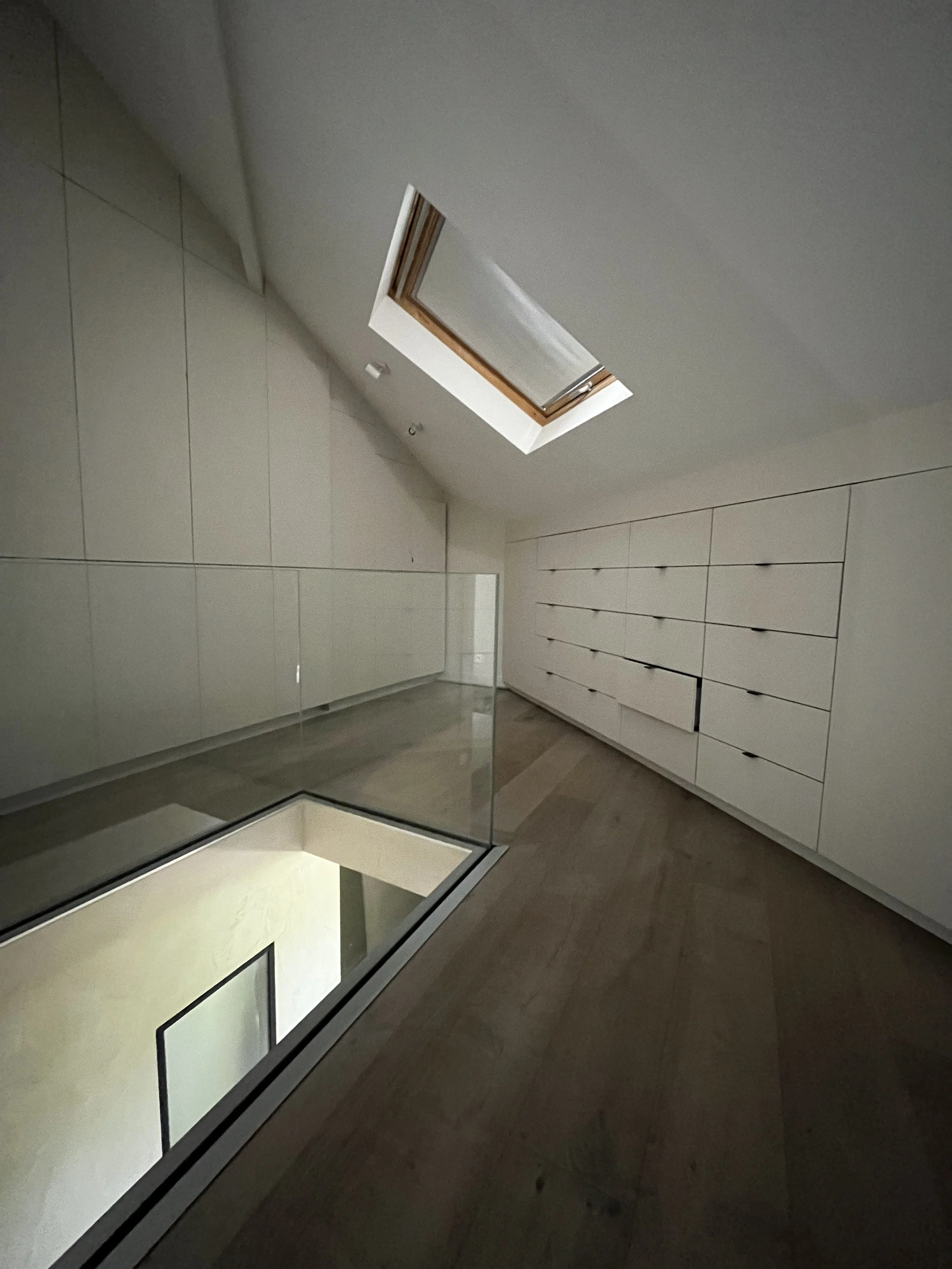 Une pièce avec un plafond en pente, un vasistas dans le plafond, des armoires blanches et un sol en bois