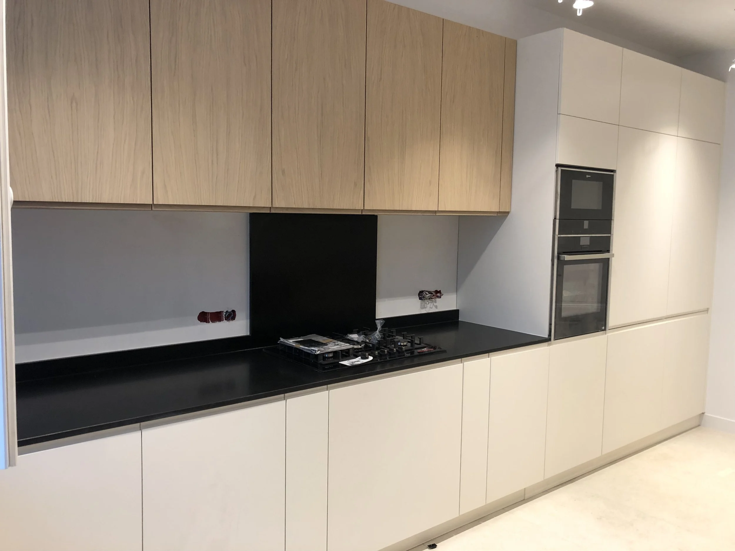 Cuisine moderne avec armoires en bois clair et un plan de travail noir. Évier, four, micro-ondes encastré, plaques de cuisson et autres appareils électroménagers intégrés. Sol en carrelage clair.
