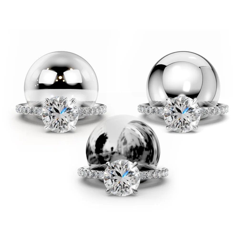 Three metallic rings, each with a large central diamond and smaller diamonds on the band, are arranged in a triangle on a white background.