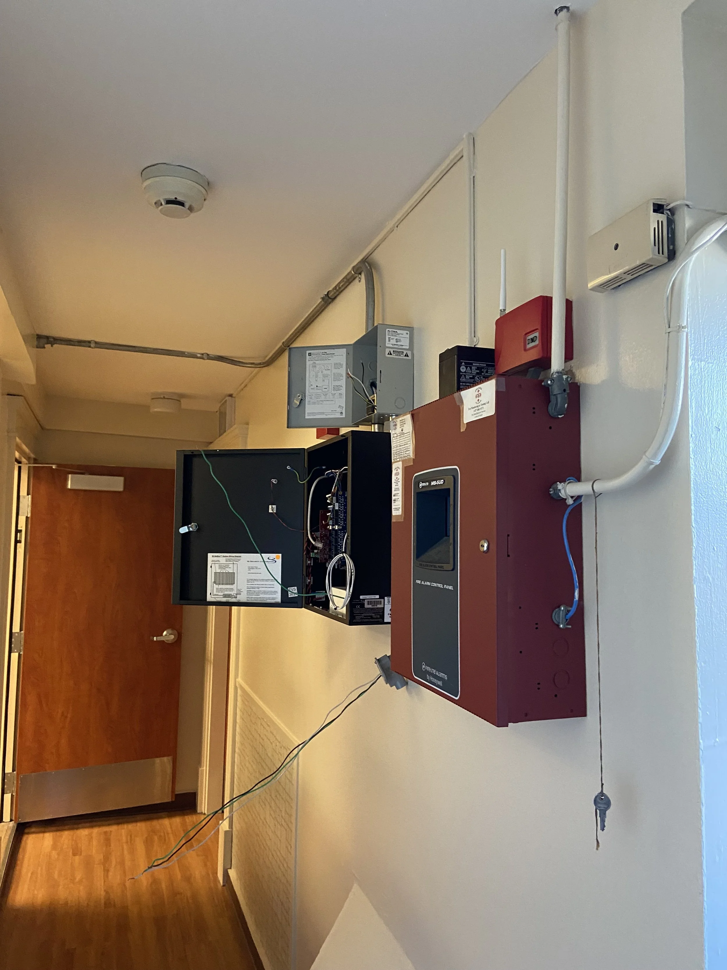 Emergency fire alarm control panel and electrical components on a wall corridor.