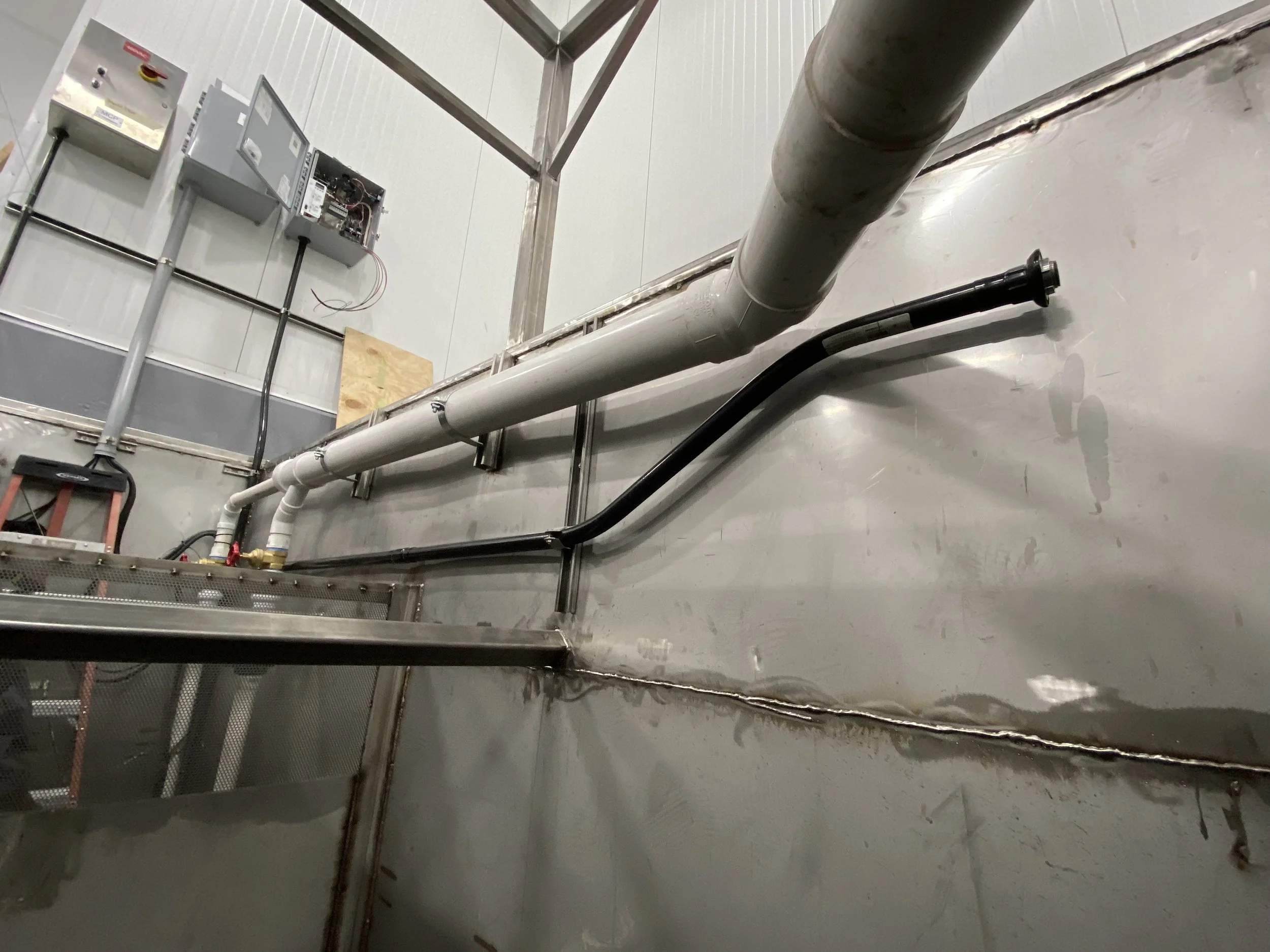 A utility room with electrical panels, plumbing pipes, and metal walls and ceiling.