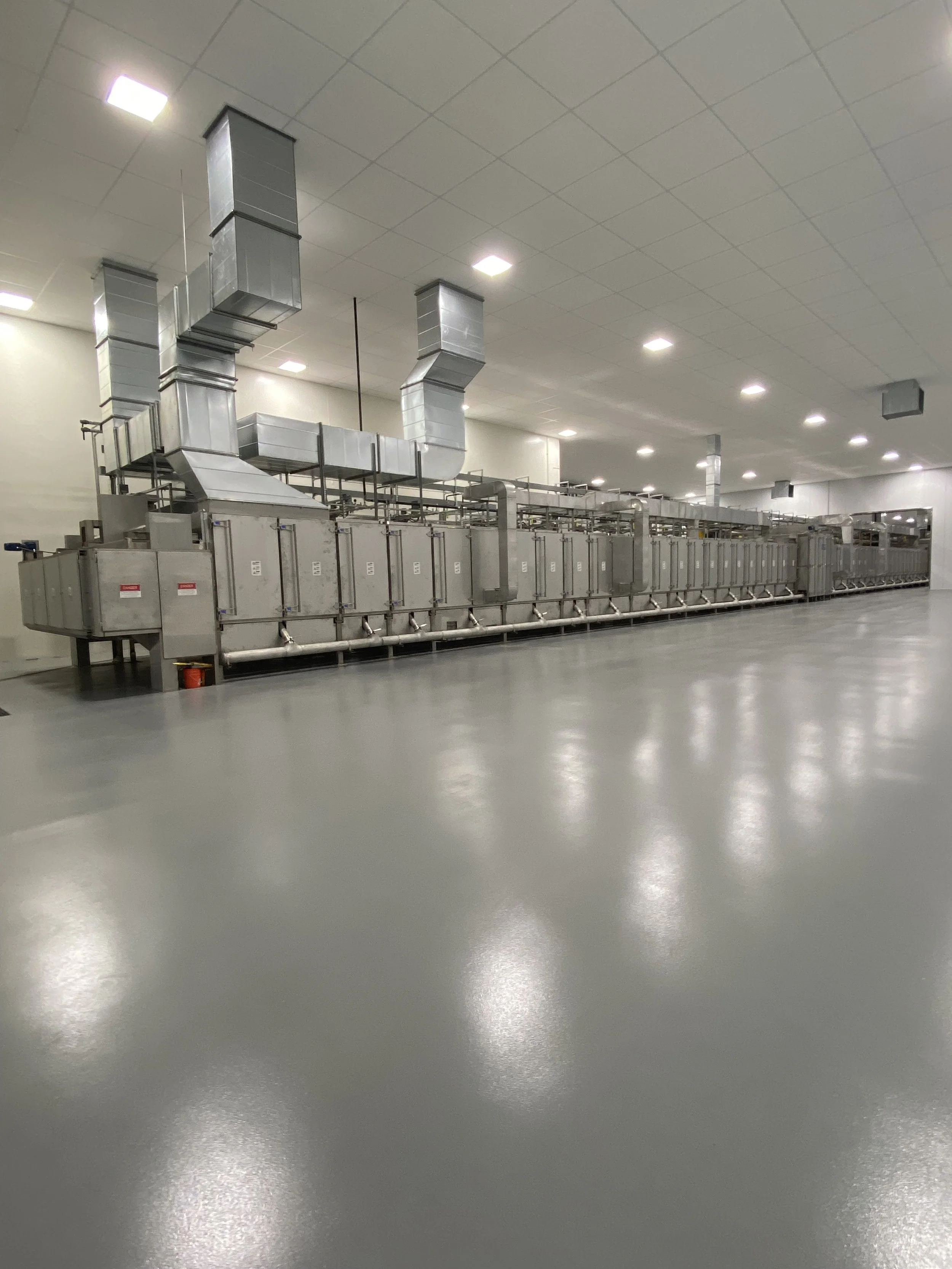 Large industrial machine with metal ducts and components in a spacious, well-lit room with a smooth gray floor.
