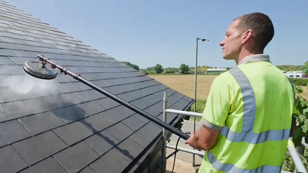 Man in a yellow safety vest pressure washing a tiled roof.