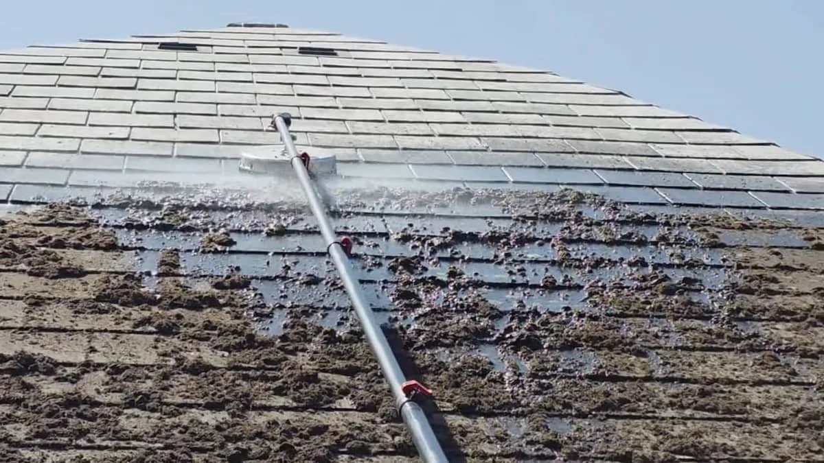 Professional roof cleaners using specialized equipment to wash away heavy moss from grey roof tiles in Earley.