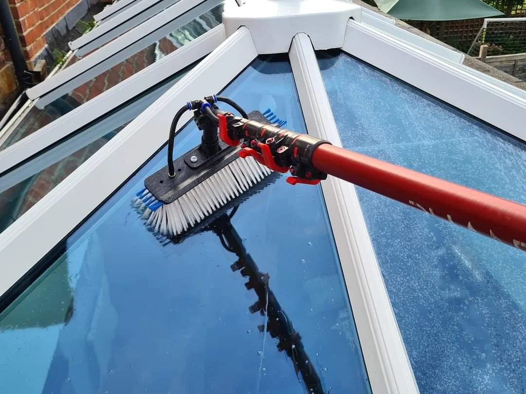 Cleaning a glass roof or window using a brush attached to a long pole.