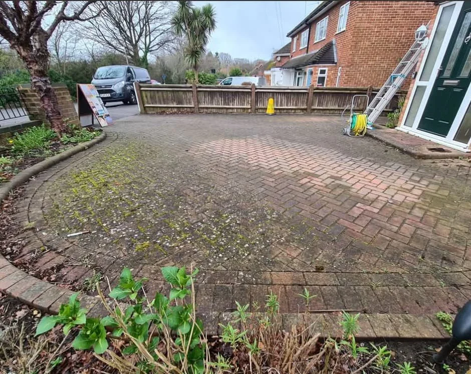 Dirty brick driveway covered in dark moss and mud with a professional jet washer machine on-site in Woodley before cleaning.
