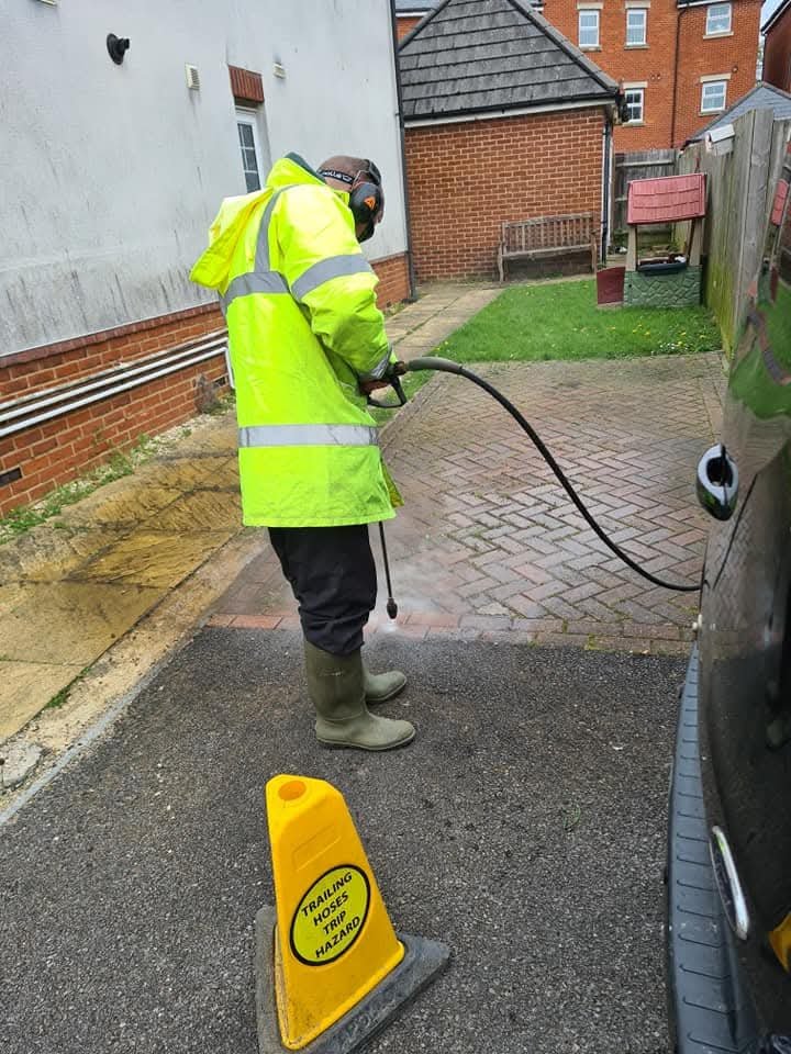 Immaculate Services wearing all PPE including face mask and high vis jacket whilst applying biocide treatment and pressure washing to driveway in Reading. Long cables trailing yellow safety cone visible