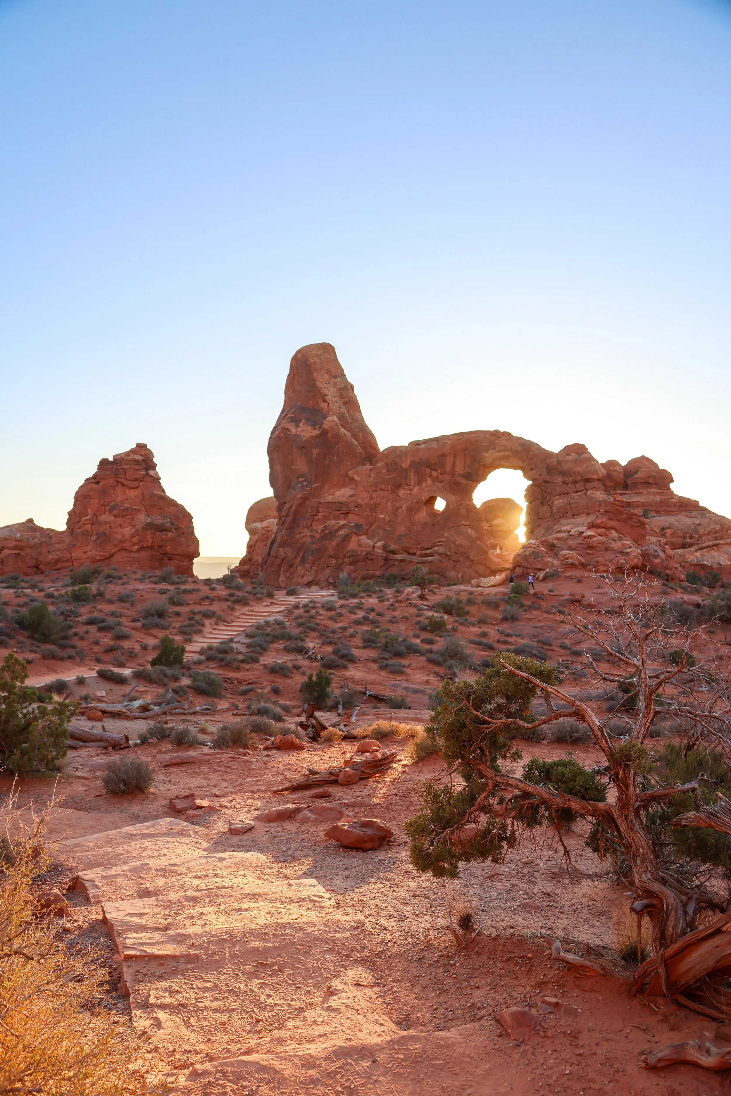 Sunset over the desert landscape with rock formations and a natural arch in Arches National Park.