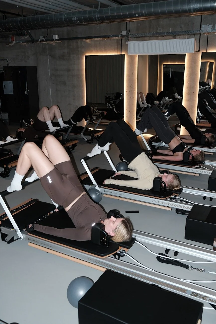 Group of women participating in a redo fitness class on reformer machines in a modern gym with mirrored walls and ambient lighting.