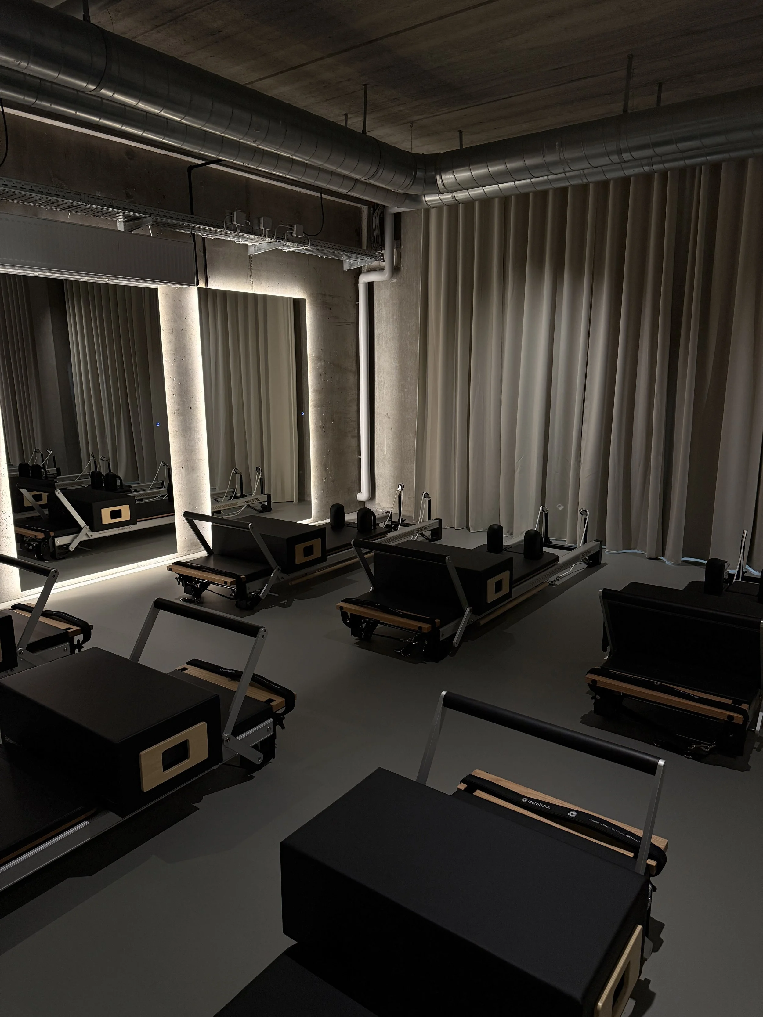 Gym with Pilates reformer machines, exercise equipment, and a modern industrial design with exposed ductwork.
