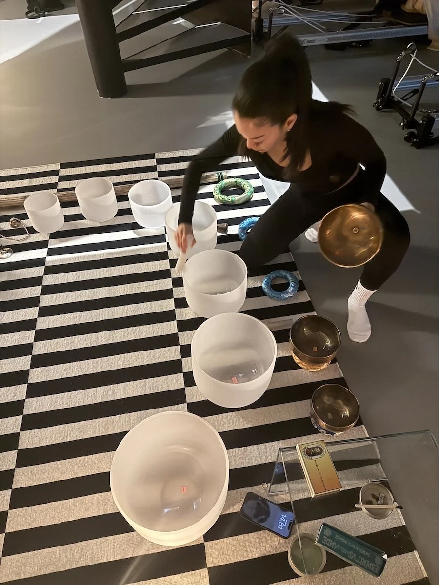 A woman arranged multiple crystal singing bowls on a black and white striped rug, preparing for a sound healing session.