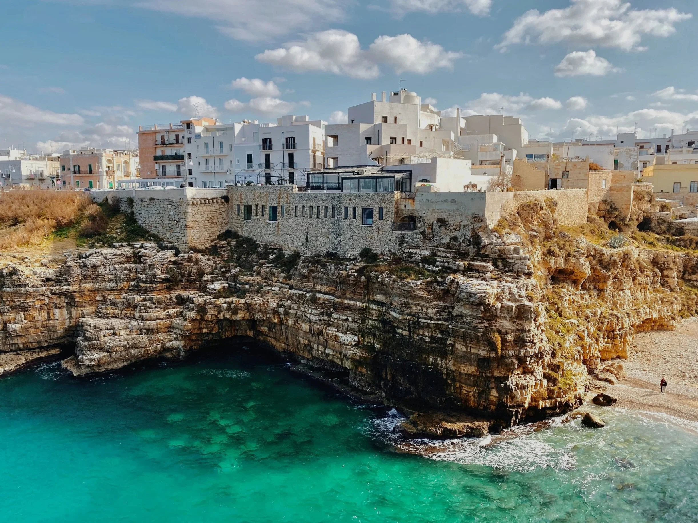 Cliffside buildings overlooking a turquoise sea with a sandy beach at the base.