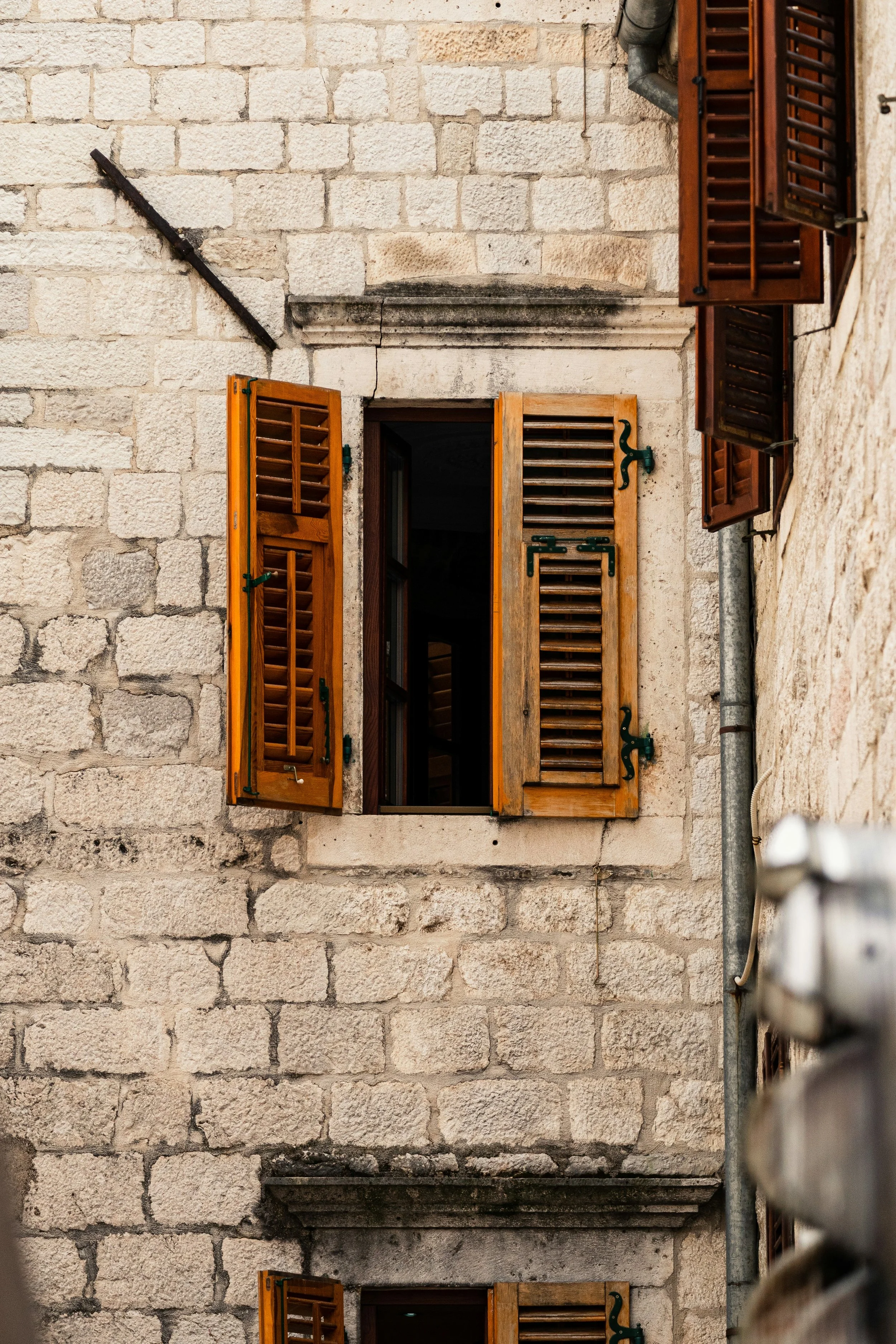 Stone building with open wooden window shutters, some with louvered slats, on a brick wall.