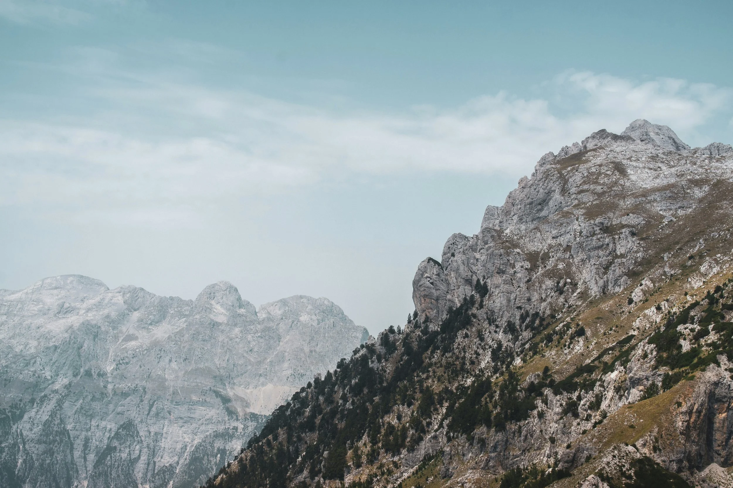 A mountain landscape with rocky peaks and patches of forest under a partly cloudy sky.