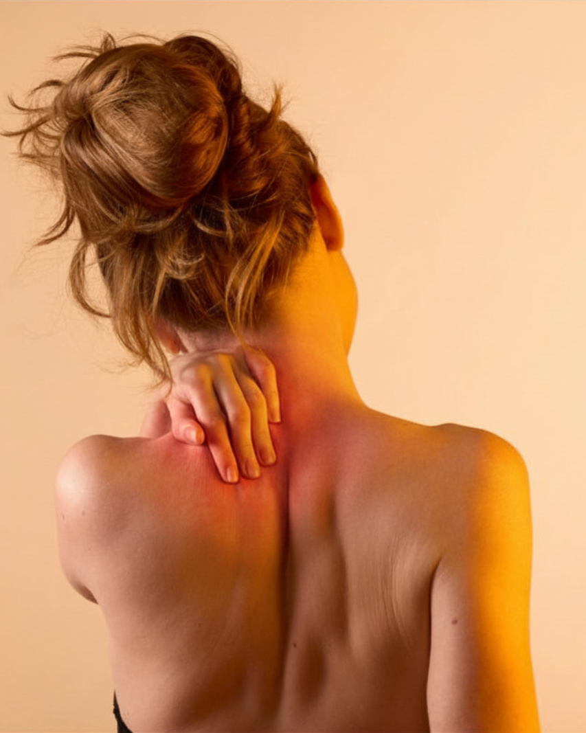 Femme vue de dos, la main posée sur la nuque et l’épaule, évoquant des douleurs cervicales et musculaires.