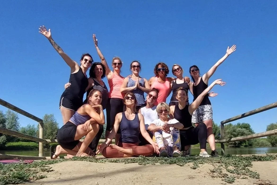 Groupe de femmes posant ensemble à l'extérieur lors d'une journée ensoleillée, avec un ciel bleu clair et un environnement naturel en arrière-plan.