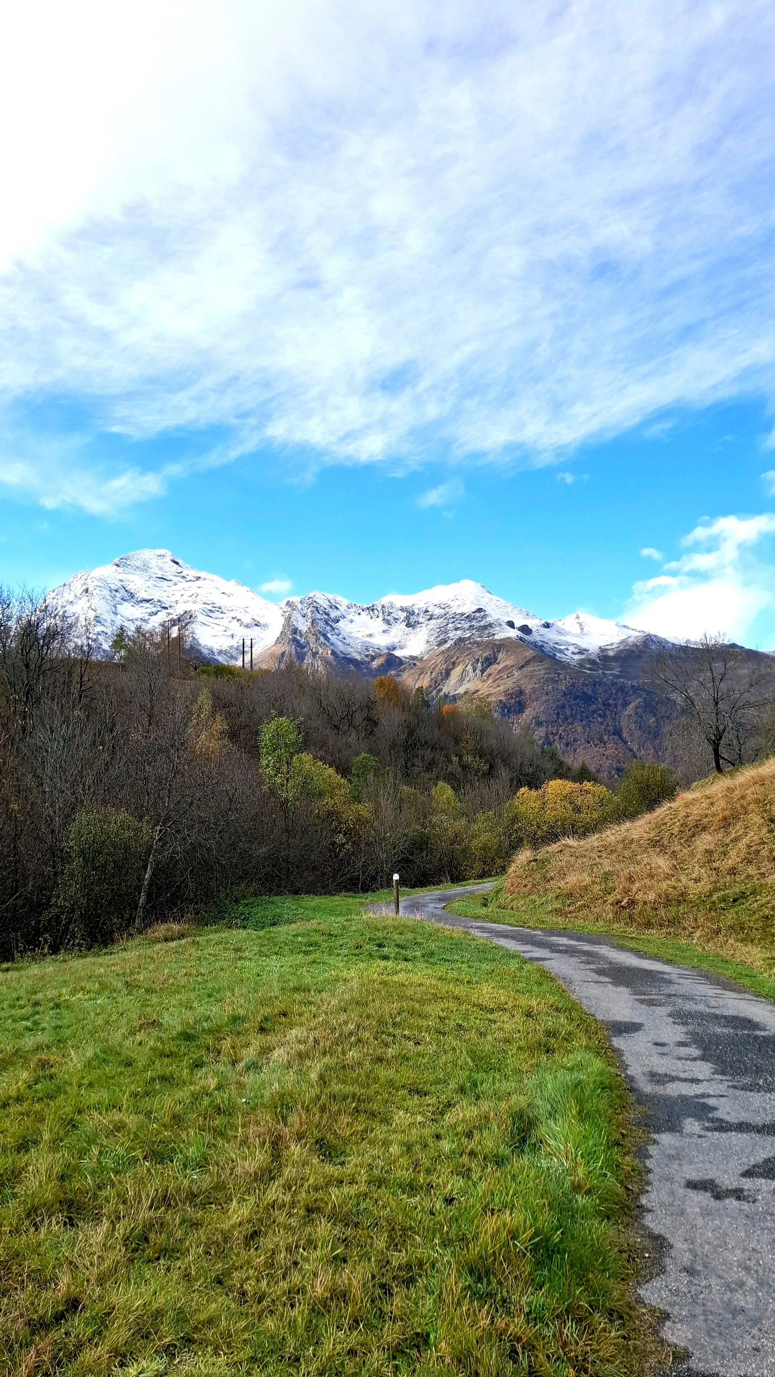 Un chemin de campagne serpentant vers des montagnes enneigées sous un ciel partiellement nuageux.