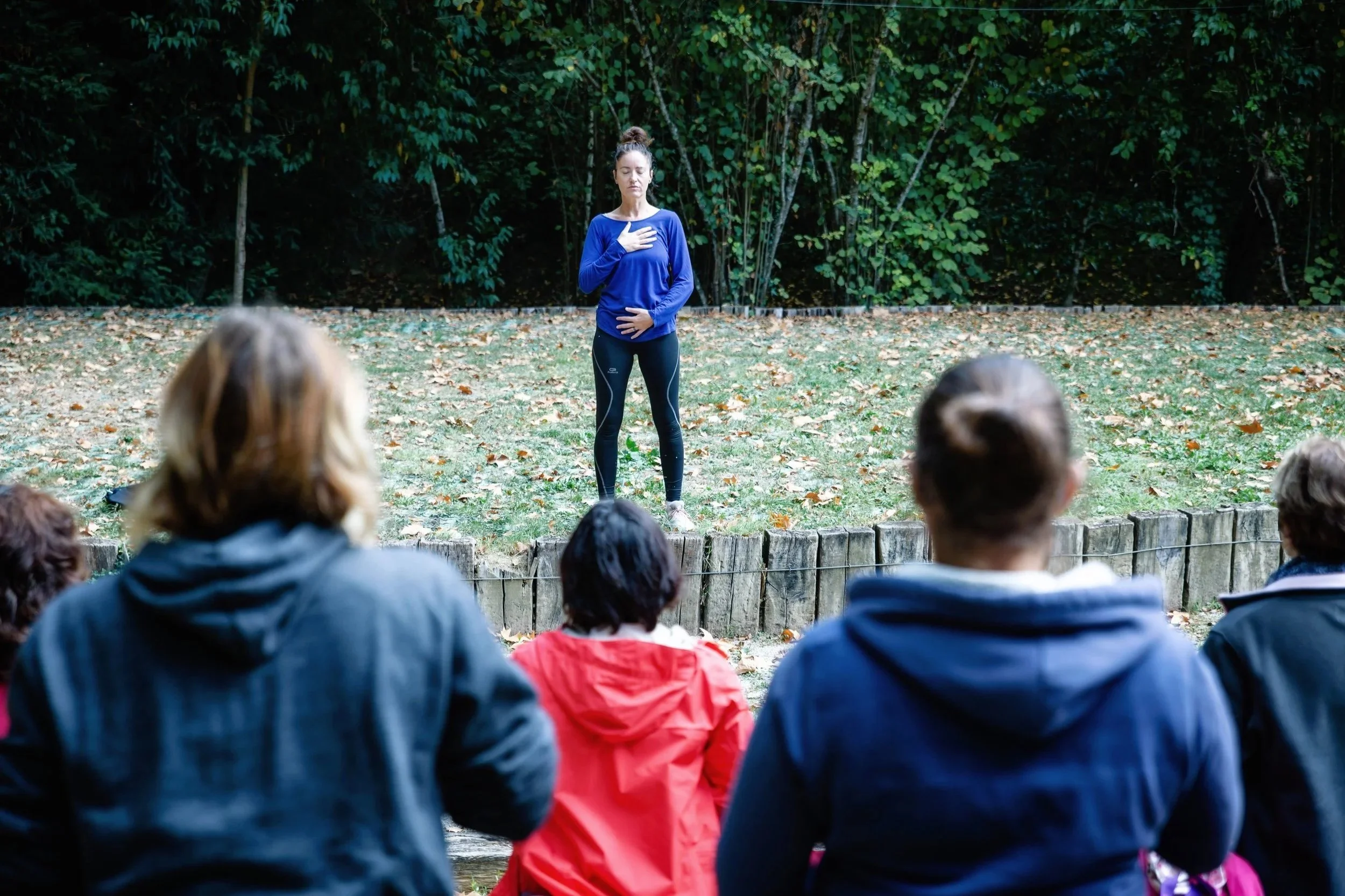 Une femme en tenue de sport faisant une activité de respiration ou de méditation devant un groupe de personnes en plein air, dans un parc.
