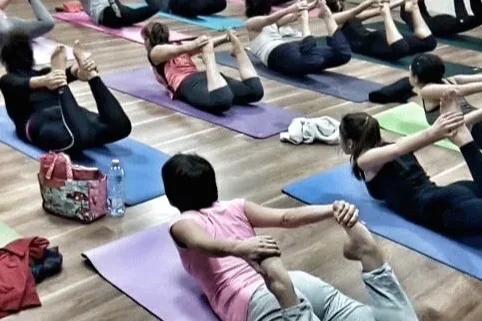 Groupe d'élèves participant à un cours de yoga en intérieur, allongées sur des tapis de yoga, en position de l'Arc flexion avec les bras tendus
