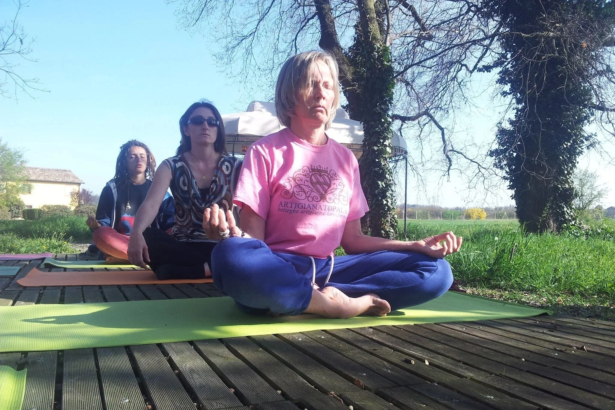 Élèves pratiquant la méditation en pleine nature sous un arbre, assises sur des tapis de yoga, avec un ciel dégagé derrière.
