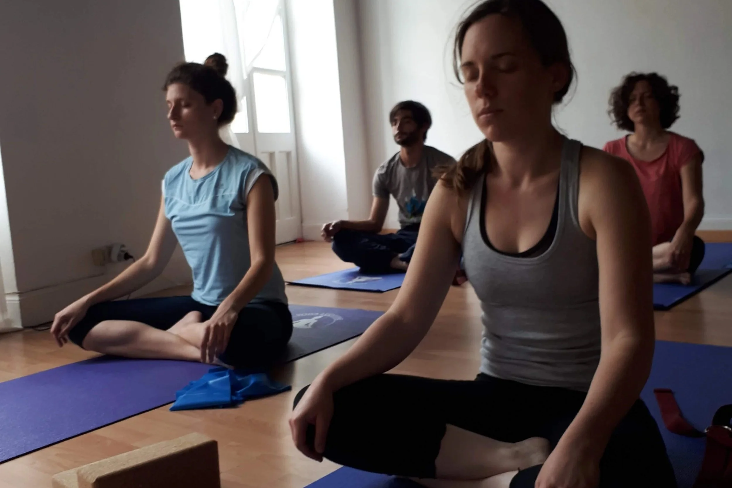 Groupe de personnes faisant du yoga en méditation, assises en position de lotus dans une pièce calme.