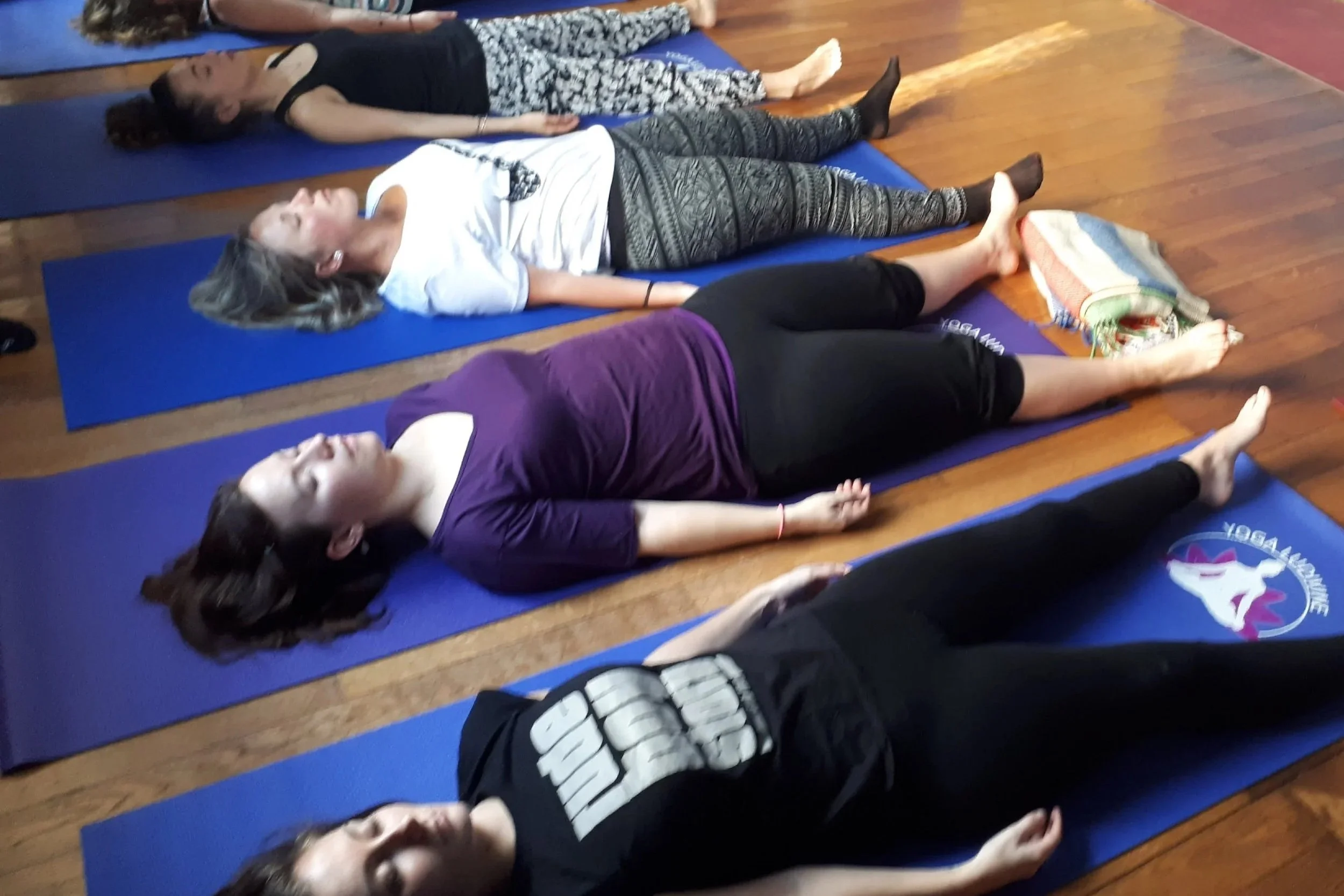 Groupe de personnes pratiquant le yoga en position de relaxation sur des tapis bleus dans une salle