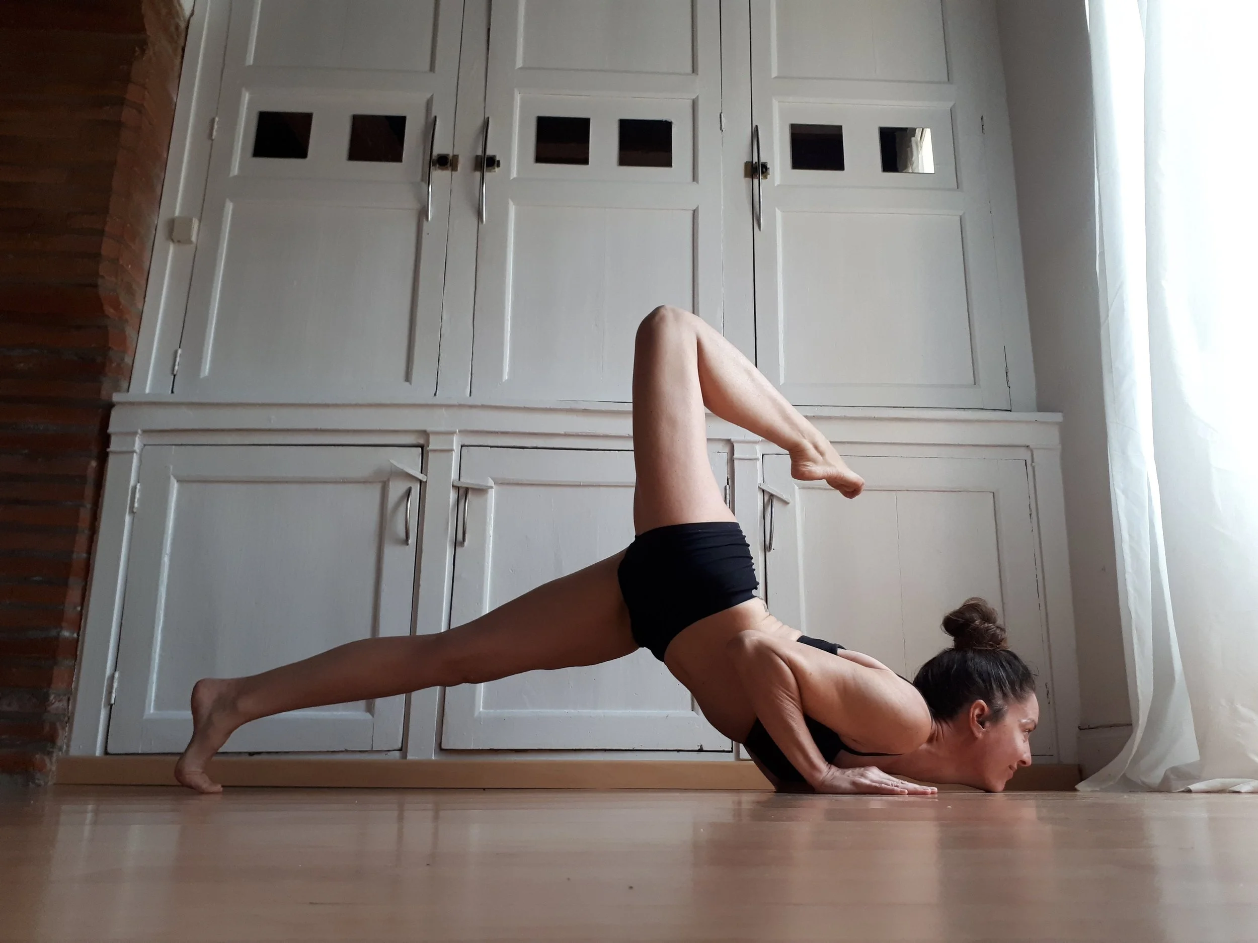 Femme faisant la posture de half chaturanga jambe levée en yoga dans une pièce lumineuse