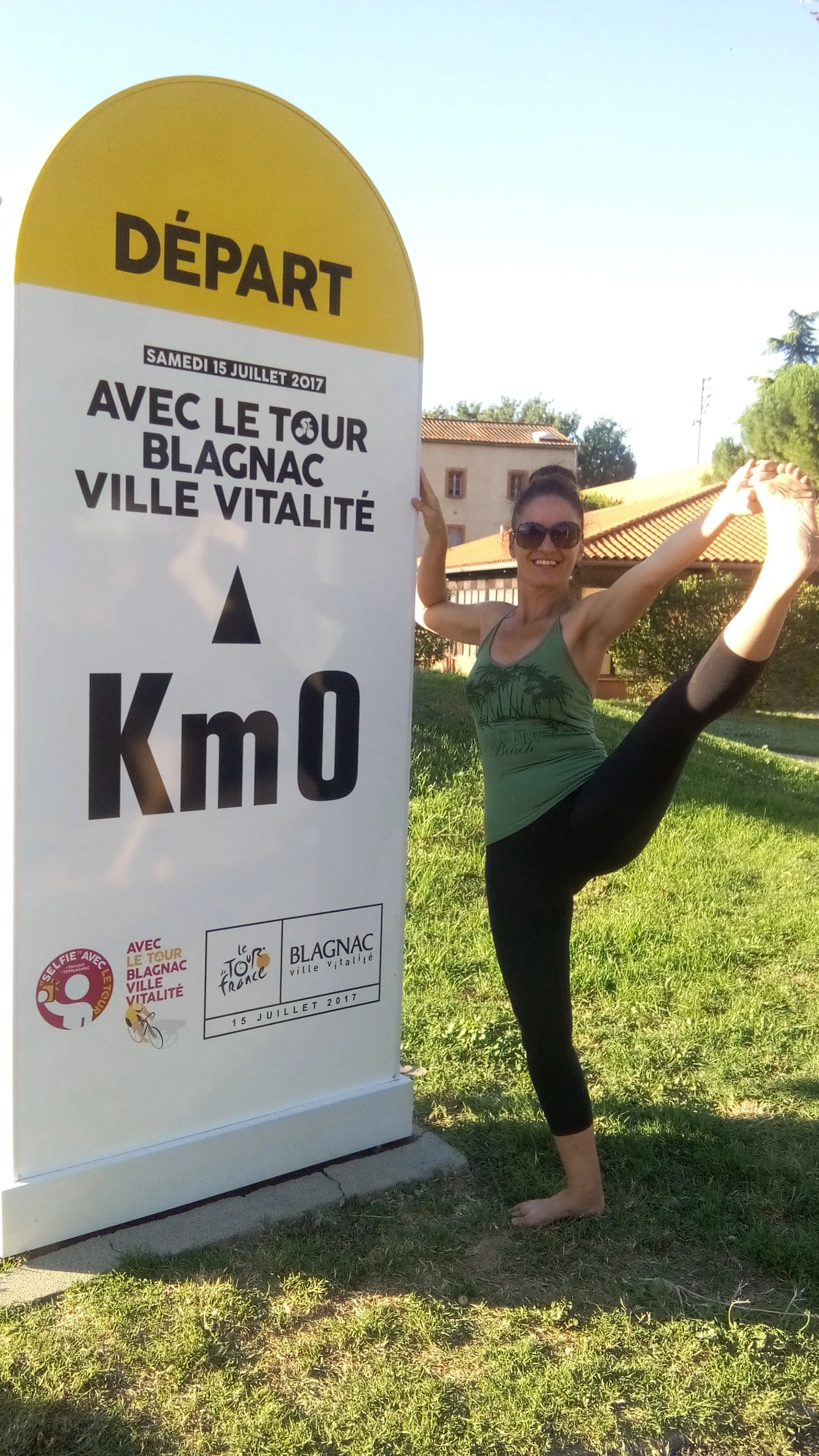Femme en yoga, faisant une posture d'étoile, à côté d'un panneau d'événement vélo dans une zone verte
