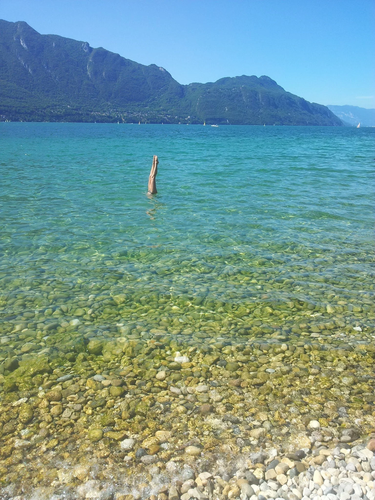 Une personne plonge la tête dans un lac transparent avec des montagnes en arrière-plan.