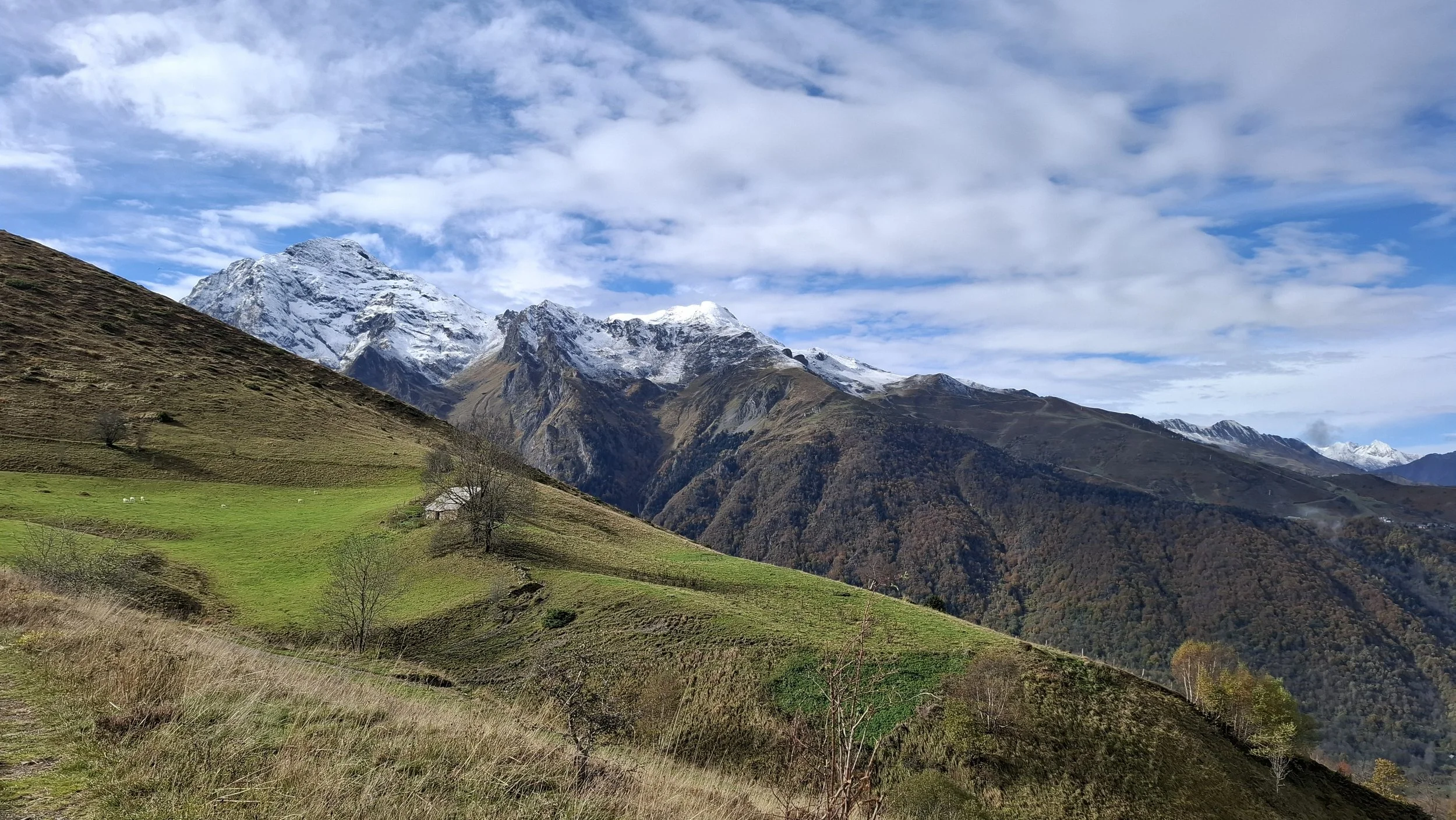 Paysage de montagnes dans les pyrénées avec sommets enneigés, collines verdoyantes et ciel partiellement nuageux. Lieu de retraite de yoga.