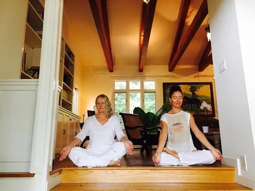 Deux femmes pratiquant la méditation ou le yoga en position de lotus à l'intérieur d'une maison lumineuse.Une donne un cours particulier á l'autre femme, Santa Barbara Californie.