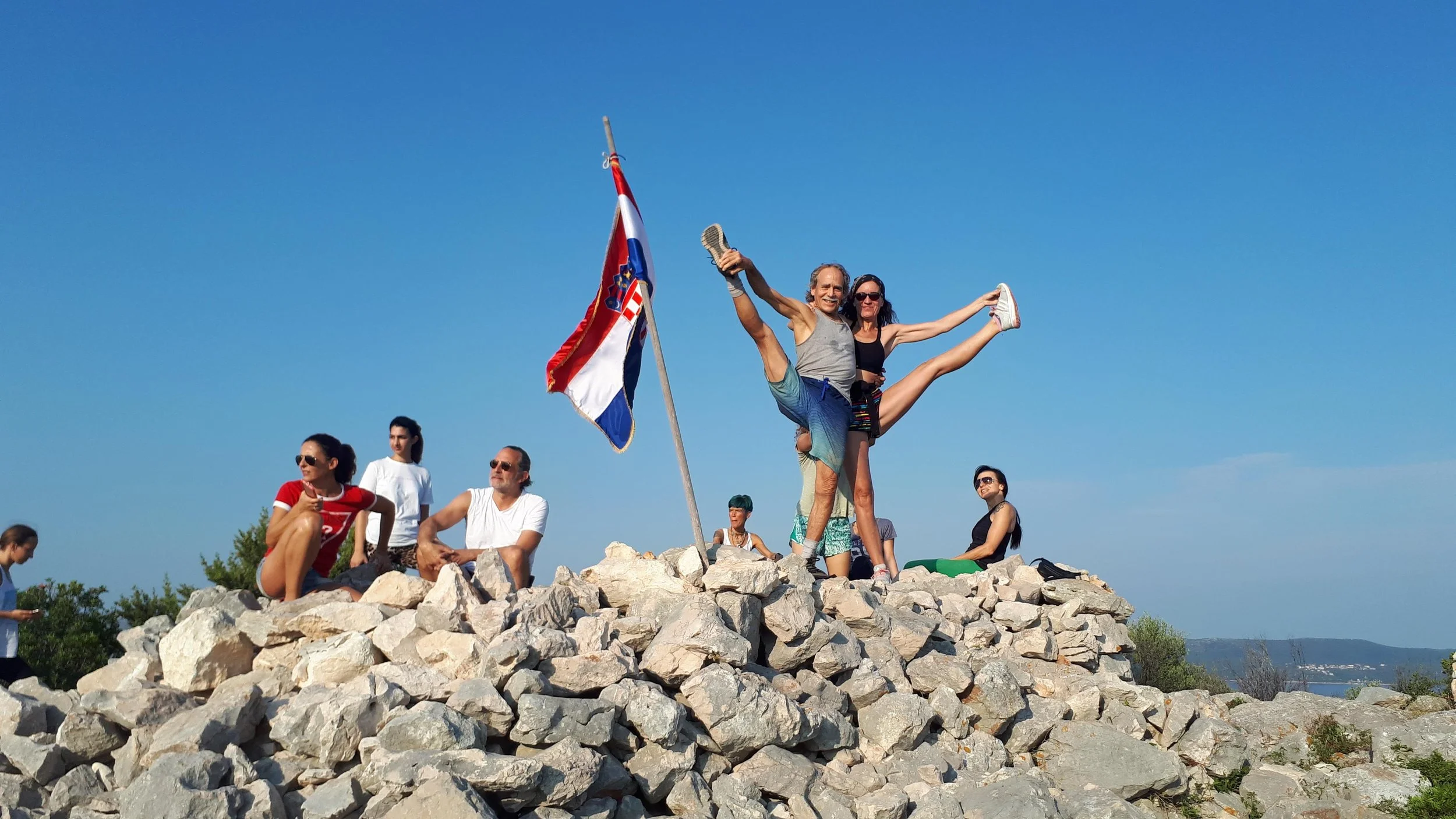 Position de yoga debout. Groupe de personnes devant un drapeau croate sur une pile de pierres, en plein air, ciel bleu.