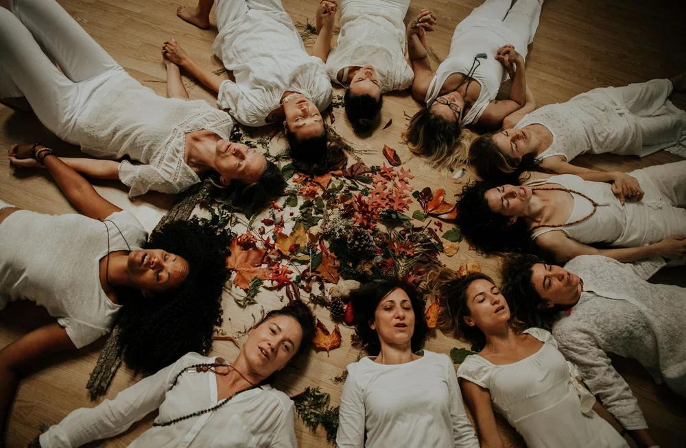 Groupe de yogis allongées en cercle sur un sol en bois, entourant des feuilles et des éléments de décoration automnale. Cérémonie de la formation de professeur de yoga.
